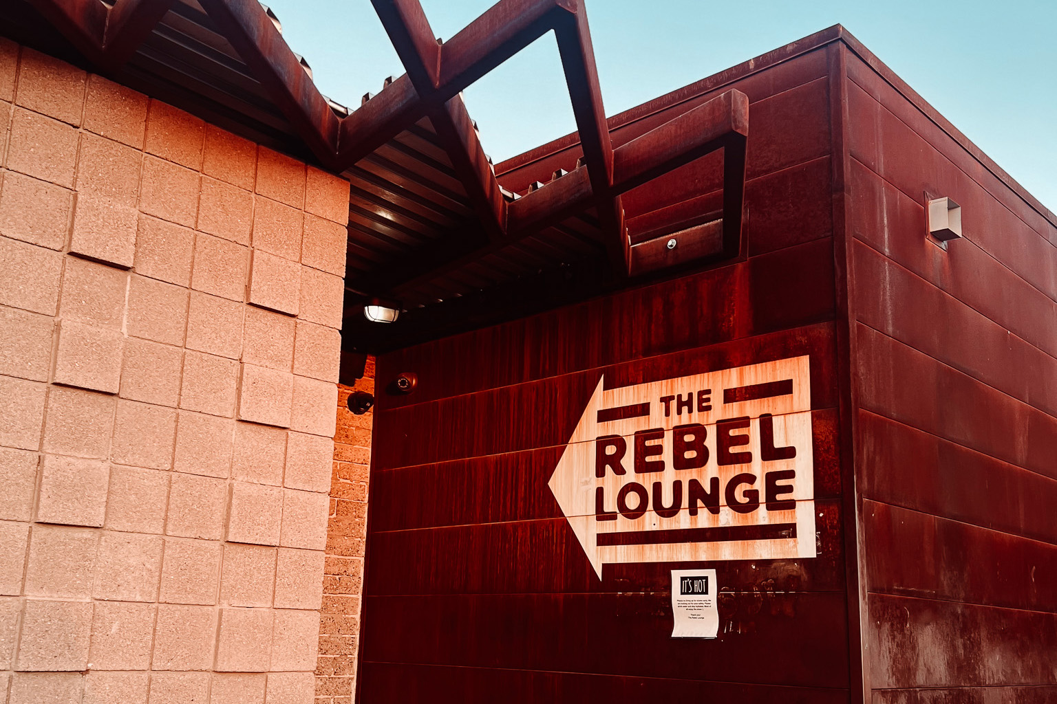 A brick wall painted with a Rebel Lounge entrance sign under a blue sky.